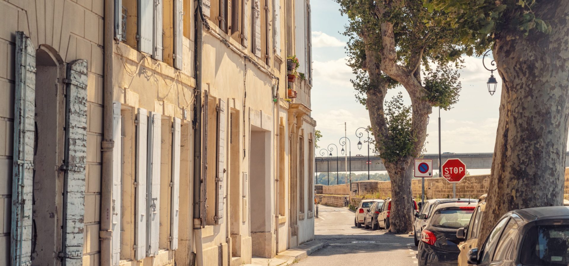 Sunlit street with historic buildings and trees in Arles, France